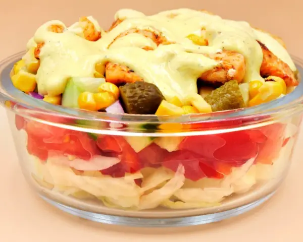Sałatka gyros w szklanej misce z kurczakiem, kukurydzą, ogórkiem i sosem.