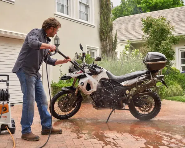 Uomo lava moto a idropulitrice in giardino. Ecco come lavare la moto a casa per mantenerla splendente.