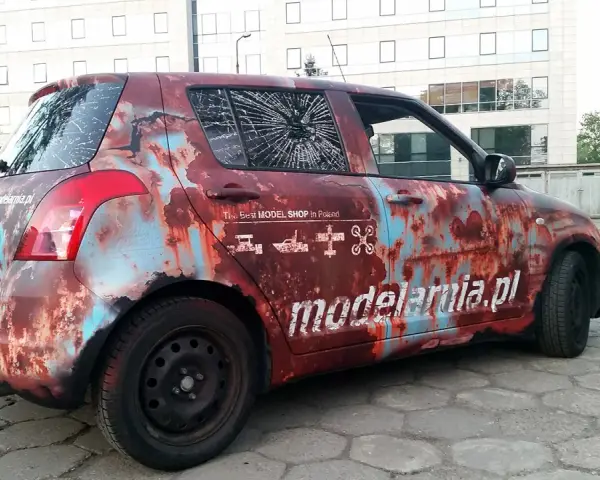 Samochód z okleiną imitującą rdzę, z napisem "modelarnia.pl" i ikonami modeli. Reklama na samochodzie zarobek.