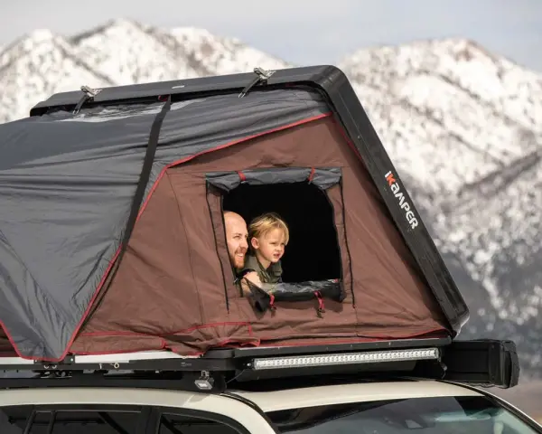 Vater und Kind schauen aus einem Dachzelt. Ein Abenteuer im Winter mit dem Dachzelt ist möglich.