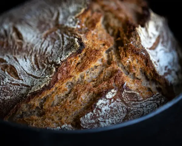 Frisch gebackenes Brot mit knuspriger Kruste ruht auf Backpapier im Gusseisentopf.