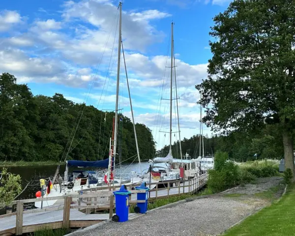 Segelbåtar vid kajen på Dalbergså camping. Grönskande träd och en blå himmel med moln.