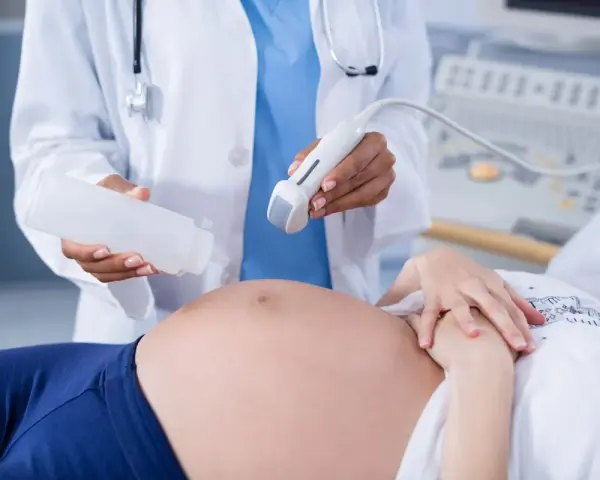 Badania prenatalne w 12 tygodniu ciąży: lekarz aplikuje żel na brzuch pacjentki przed badaniem USG.