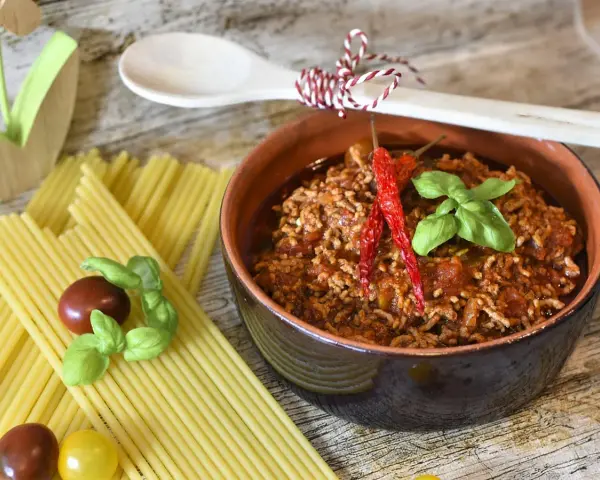 Un invitante ragù, pronto per la pasta, con peperoncini e basilico. La ricetta perfetta per un pranzo gustoso.