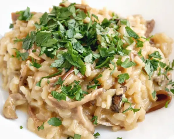 Kremowe risotto z grzybami, posypane świeżą natką pietruszki, wygląda apetycznie.