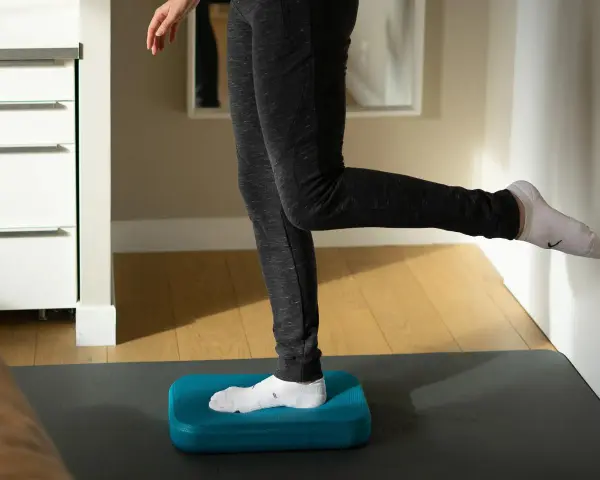 Personne effectuant des exercices de renforcement de la cheville sur un step bleu, idéal pour la rééducation après une entorse.