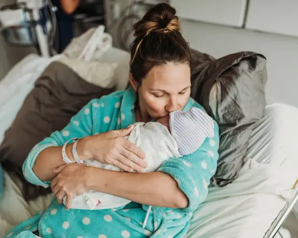 Mama tuli dziecko po cesarce, czule całując je w czapeczkę. Laktacja po cesarce może być wyzwaniem, ale miłość jest silniejsza.