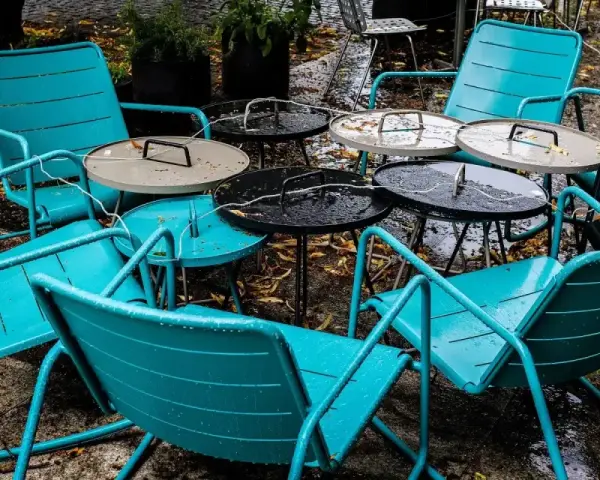 Teal metal chairs and tables, perfect for outdoor use, sit empty on a wet patio.