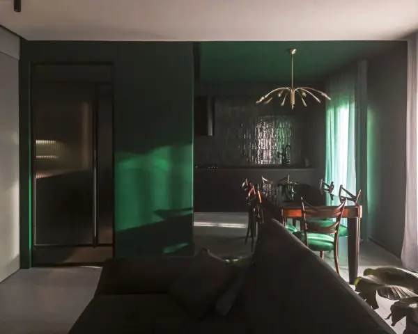 Un soggiorno moderno con pareti verde scuro, un divano antracite e una zona pranzo con sedie verdi. I colori da abbinare al verde scuro sono il legno scuro e l'ottone.
