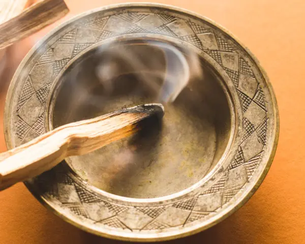 Humo ascendente de un palo santo quemándose en un cuenco metálico. Descubre a qué huele el palo santo.