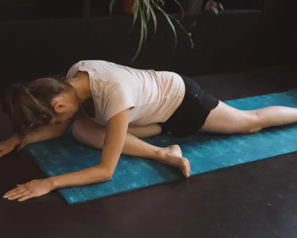 Femme en posture de pigeon sur un tapis bleu, un excellent exercice pour le dos à la maison.