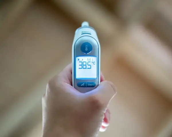 Cyfrowy termometr pokazuje 38.5°C, co oznacza stan podgorączkowy.