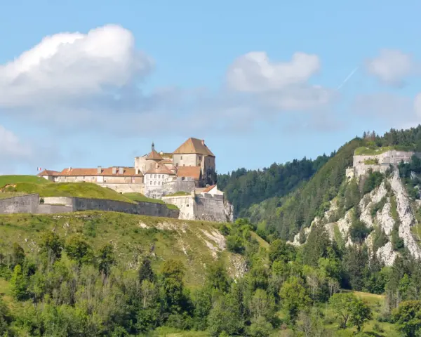 Fort de Joux, un site historique à visiter dans le Doubs, perché sur une colline verdoyante sous un ciel bleu.