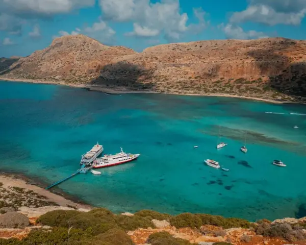 Wycieczka na Santorini z Krety: statki cumują w turkusowej zatoce, otoczonej skalistymi wzgórzami.