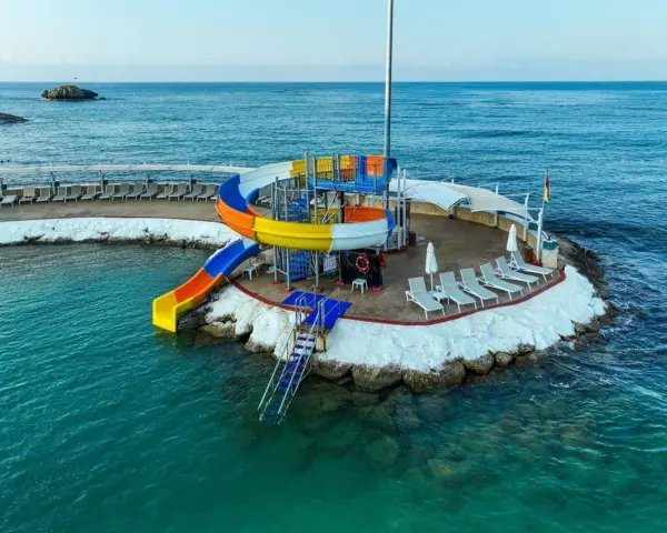 Kolorowe zjeżdżalnie wodne i leżaki na wyspie w Orange County Alanya, nad turkusowym morzem.