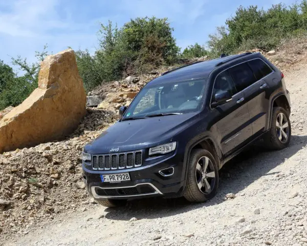 Schwarzer Jeep Grand Cherokee 3.0 CRD 250 PS im Gelände. Ein großer Felsbrocken liegt daneben.