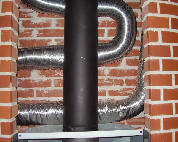 Mur brique réfractaire derrière poêle, avec conduits métalliques flexibles.