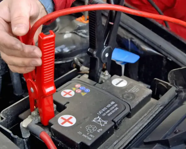 Hand befestigt rote Klemme an Autobatterie. Die richtige **Starthilfe Reihenfolge** ist entscheidend für die Sicherheit.