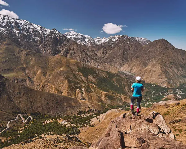 Widok na ośnieżone szczyty górskie Jebel Toubkal. Turystka podziwia panoramę z skalistego zbocza.