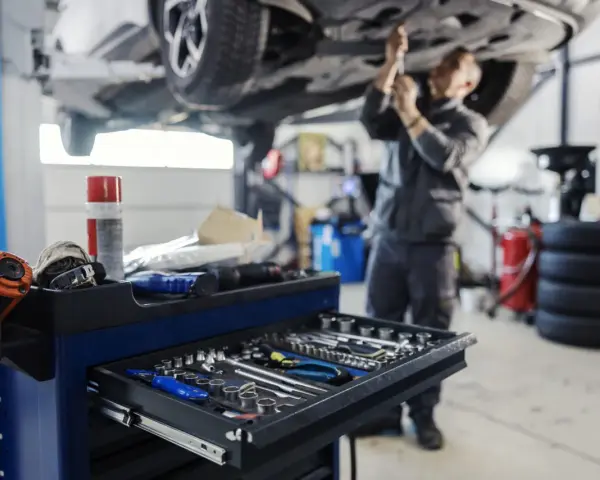 Warsztat samochodowy: mechanik pracuje pod podniesionym autem, wózek z narzędziami na pierwszym planie.