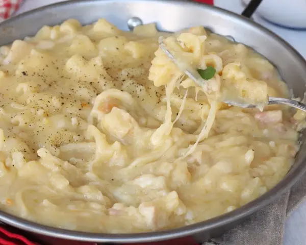 Una padella piena di cremosa pasta con patate, condita con pepe nero. Un piatto confortante e saporito.