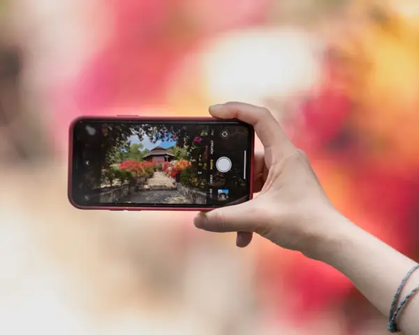 Une main tient un smartphone pour capturer un escalier fleuri menant à un pavillon. L'écran montre les bases de la photographie, avec des options comme "PHOTO" et "PORTRAIT".