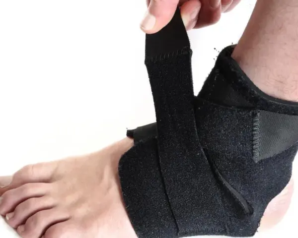 Dłoń zapina czarną ortezę na stopę, zapewniając wsparcie i stabilizację.
