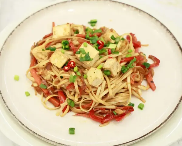 Smażony makaron Chow Mein z tofu, papryką i szczypiorkiem na talerzu.