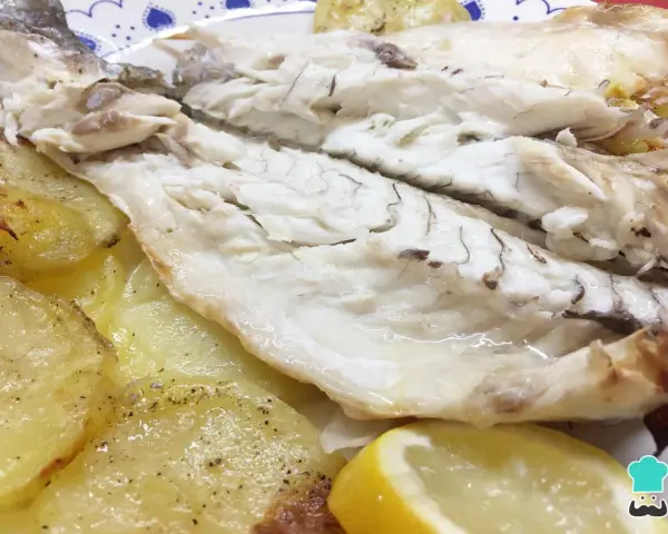 Lubina al horno jugosa y tierna, acompañada de patatas asadas y rodajas de limón fresco.