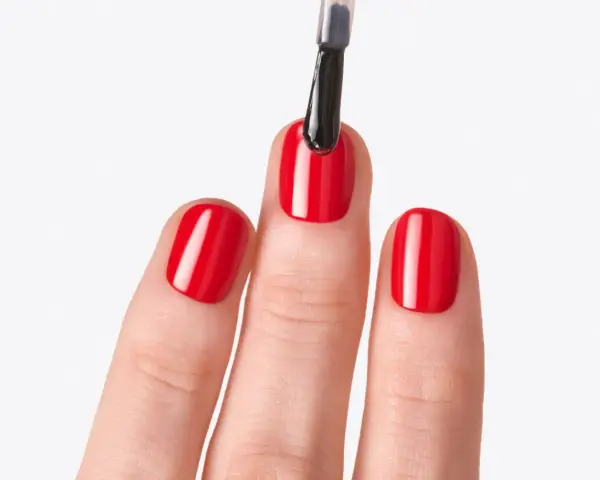 Application d'un top coat sur des ongles rouges brillants. Le top coat, c'est quoi ? C'est la touche finale pour une manucure parfaite.