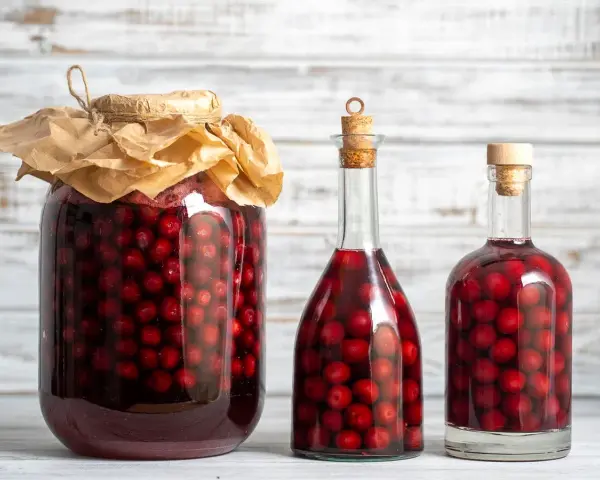 Ein großes Glas und zwei Flaschen gefüllt mit Kirschen und Alkohol. Perfekt für ein schnaps selber machen rezept.