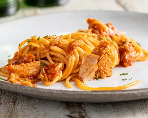 Spaghetti al tonno conditi con un sugo saporito e ricchi pezzi di tonno, guarniti con prezzemolo fresco.