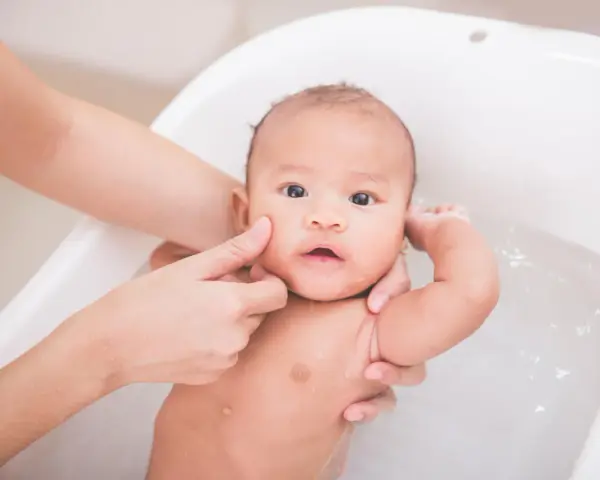 Delikatna kąpiel niemowlaka w wanience. Czy można myć dziecko z gorączką? Tak, ale w letniej wodzie, by pomóc mu się ochłodzić.