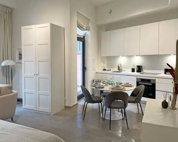 Acogedor cocina salón comedor de 30 m2 con muebles blancos, mesa redonda y sofá.
