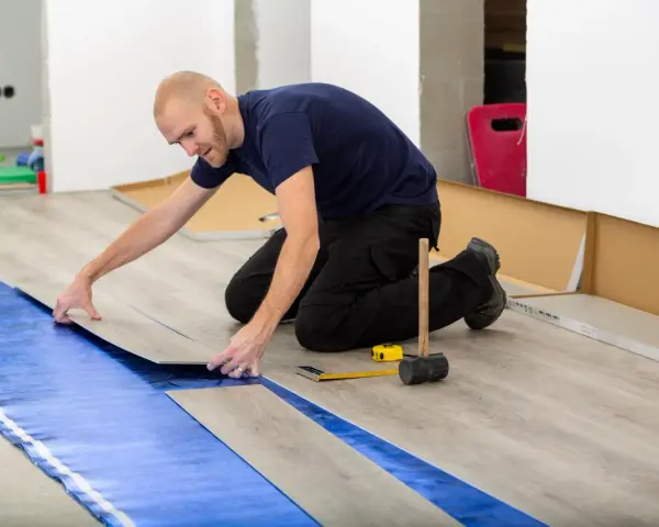 Pose d'un revêtement de sol stratifié sur une sous-couche d'isolation phonique sous carrelage. Outils de pose à proximité.