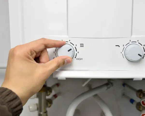 Mano girando el dial del termo eléctrico para cerrar la llave de paso.