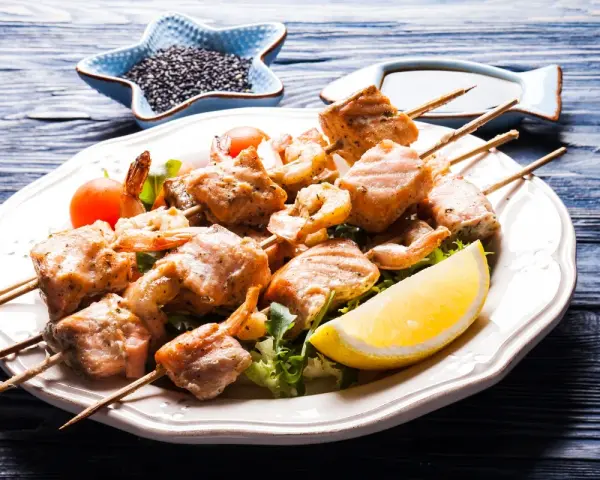 Spiedini di pesce succulenti, con gamberi e salmone grigliato, serviti su un letto di insalata con spicchio di limone.