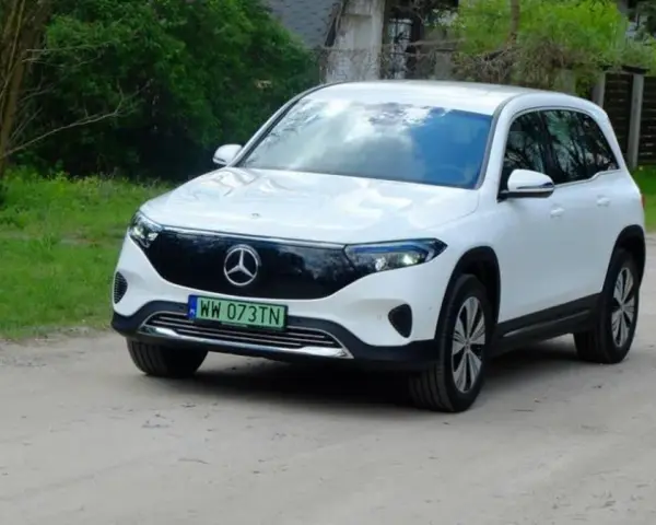 Biały Mercedes EQB na drodze gruntowej, otoczony zielenią.