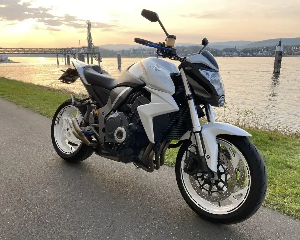 Biały motocykl Honda CB1000R, model a2 motor, zaparkowany nad rzeką o zachodzie słońca.