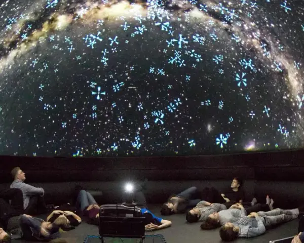 Besucher im Planetarium Berlin liegen und sitzen und blicken gebannt auf die Projektion der Milchstraße und funkelnder Sterne.