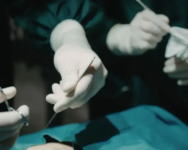 Dłonie chirurga w rękawiczkach trzymające narzędzia chirurgiczne i gazę.