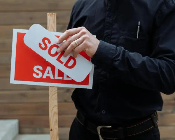 Hombre coloca cartel de "Vendido" sobre uno de "En Venta". Una venta rápida, quizás por debajo del valor de referencia.