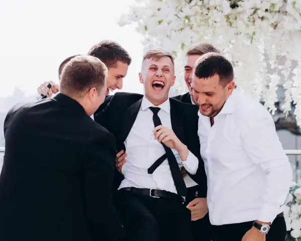 Śmiejący się pan młody otoczony przez przyjaciół. Świetne kawalerski pomysły na wspólne chwile przed ślubem.