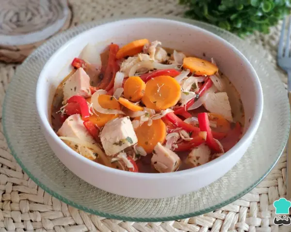 Pechuga de pollo en escabeche con zanahoria, pimiento rojo y cebolla, servida en un cuenco blanco sobre una base tejida.