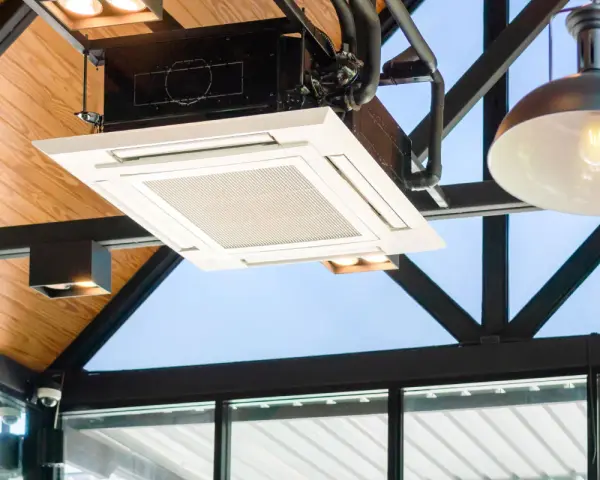 Unidad de cassette de un sistema VRV integrada en un techo de madera y metal, con luces y tuberías visibles.