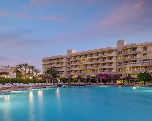 Basen i hotel o zachodzie słońca. Wiele leżaków i palm. Idealne miejsce na wakacje, zgodnie z licznymi sindbad club opinie.
