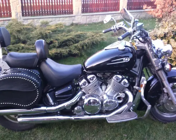 Czarny motocykl Yamaha Royal Star z chromowanymi detalami i skórzanymi sakwami, zaparkowany na trawie przed płotem.