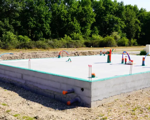 Betonowe fundamenty pod dom parterowy z instalacją hydrauliczną. Zielona izolacja na obrzeżach płyty.