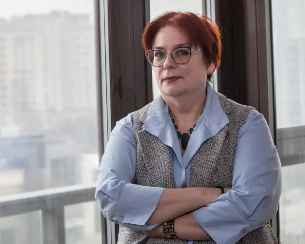 Kobieta w okularach, z rudymi włosami, opiera się o okno. Jej postawa sugeruje siłę i determinację w odpowiedzi na pytanie, jak żyć po rozwodzie.