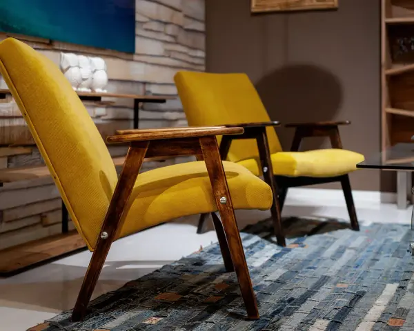 Due poltrone gialle con struttura in legno scuro, un tappeto patchwork e un tavolino in vetro. Un tocco di arredamento anni '70 italiano.
